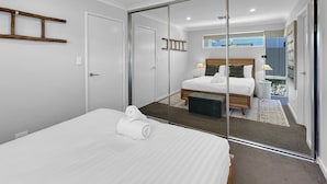 Una habitación de hotel moderna con una cama grande, un cabecero de madera, una puerta de cristal que da a un balcón y una mesita de noche con una lámpara.
