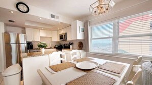 Une cuisine moderne avec des meubles blancs, des appareils en acier inoxydable et un coin repas comprenant une table et des chaises blanches.