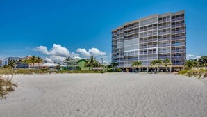 Un hôtel situé en bord de mer, doté d’un grand bâtiment, d’une plage de sable et de palmiers.