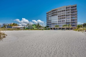 Ein Strandhotel mit einem großen Gebäude, Sandstrand und Palmen.