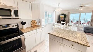 Une cuisine moderne avec des meubles blancs, un plan de travail en granit et un coin repas comprenant des chaises blanches et un téléviseur.