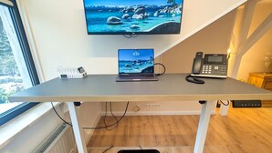 A modern home office setup with a desk, laptop, phone, and a TV displaying a scenic landscape.