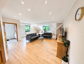 Amplia sala de estar con un sofá grande, una mesa de centro y un televisor. Ventanas que ofrecen luz natural y vistas al exterior.