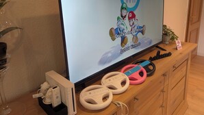 A television displaying a Mario Kart Wii game, a Wii console, and two Wii steering wheels on a wooden cabinet.