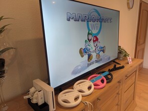 A television displaying a Mario Kart Wii game, a Wii console, and two Wii steering wheels on a wooden cabinet.
