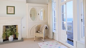A room with a fireplace, a wicker chair, a large mirror, and a view of the sea through open doors. - West Ingle Large Edwardian Home Overlooking Seagrove Bay (Seaview)