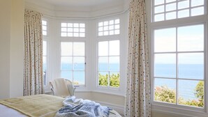 A bedroom with a large bed, a view of the sea, and a chair by the window. - West Ingle Large Edwardian Home Overlooking Seagrove Bay (Seaview)