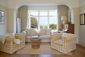 A living room with a checkered sofa set, a wicker coffee table, and a piano. - West Ingle Large Edwardian Home Overlooking Seagrove Bay (Seaview)