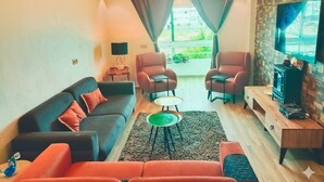 A modern living room with a sofa, armchairs, a coffee table, and a TV. - Résidence Luxueuse, 2 Piscines Escapade Familiale à 2 pas Plages Harhoura Rabat (Harhoura)