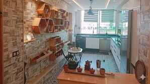 A modern kitchen with a brick wall, wooden shelves, and a dining area with a table and chairs. - Résidence Luxueuse, 2 Piscines Escapade Familiale à 2 pas Plages Harhoura Rabat (Harhoura)