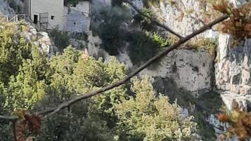 Paisatge de muntanya rocosos amb una petita construcció de pedra situada entre penya-segades i vegetació densa.