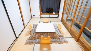 Una habitación de estilo japonés tradicional con suelo de tatami, una mesa baja con cojines y puertas correderas.