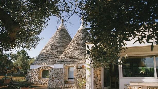 Una casa de piedra con tejados cónicos, un banco de piedra y una planta en maceta.