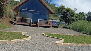 Un edificio moderno con fachada de vidrio amplia, terraza de madera y camino de entrada de grava.