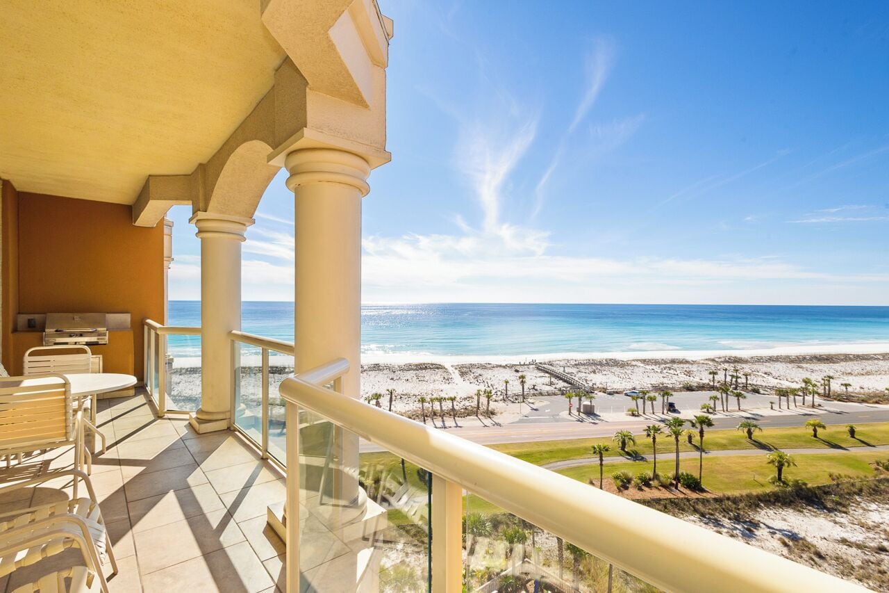 A balcony with a view of the beach, outdoor seating, and a pool area.