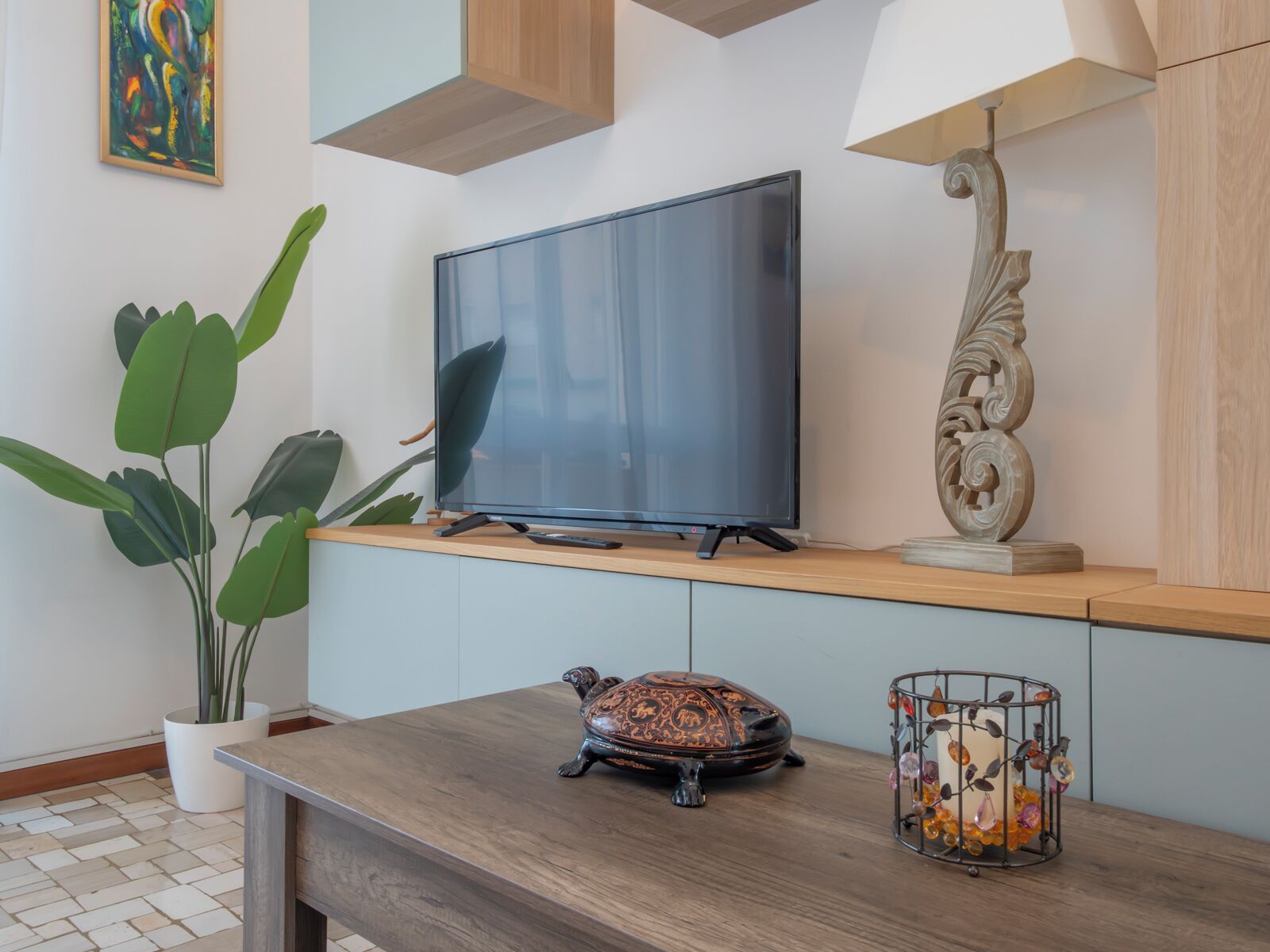 Un soggiorno moderno con una televisione a schermo piatto su una mensola in legno, una pianta in vaso, una tartaruga decorativa e una gabbia per uccelli in metallo con decorazioni.