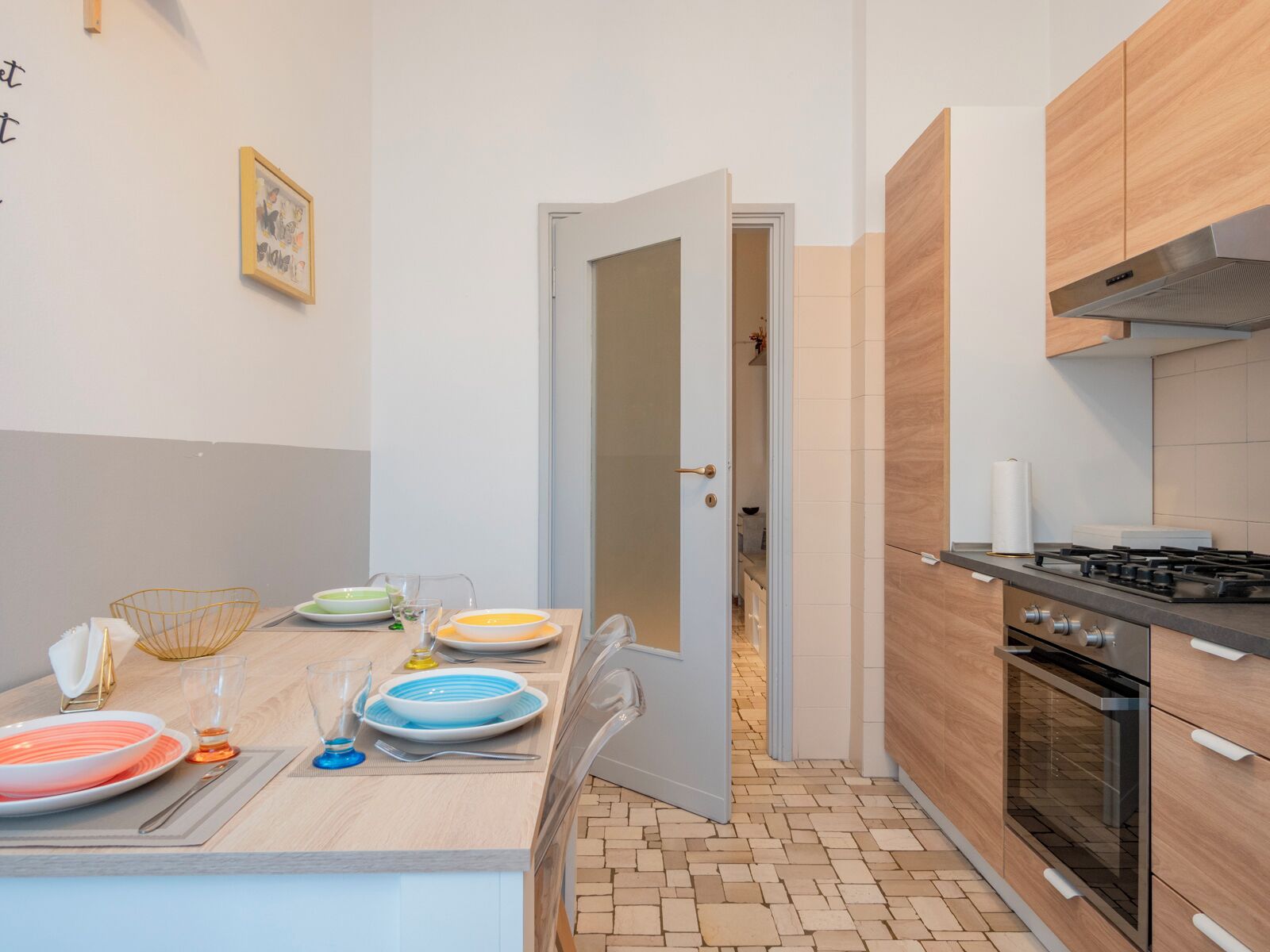 Una cucina moderna con zona pranzo, dotata di fornello, forno e tavolo imbandito con piatti e bicchieri.