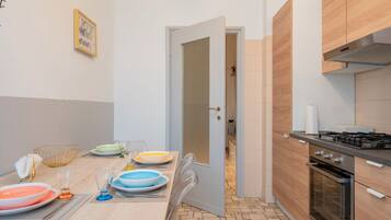Una cucina moderna con zona pranzo, dotata di fornello, forno e tavolo imbandito con piatti e bicchieri.
