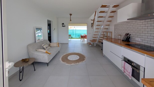 A modern kitchen with white cabinets and a wooden countertop, a grey sofa with cushions, and a staircase leading to an outdoor area. - Quiet new villa - Tropical relaxation guaranteed (Saint-François)