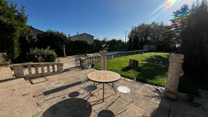 Eine Terrasse im Freien mit einem runden Tisch und Stühlen, einer Steinbrüstung und einer Rasenfläche.