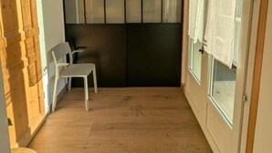 Ein Zimmer mit Holzboden, einem weißen Stuhl, einer Holztür und einem Fenster mit Vorhängen.