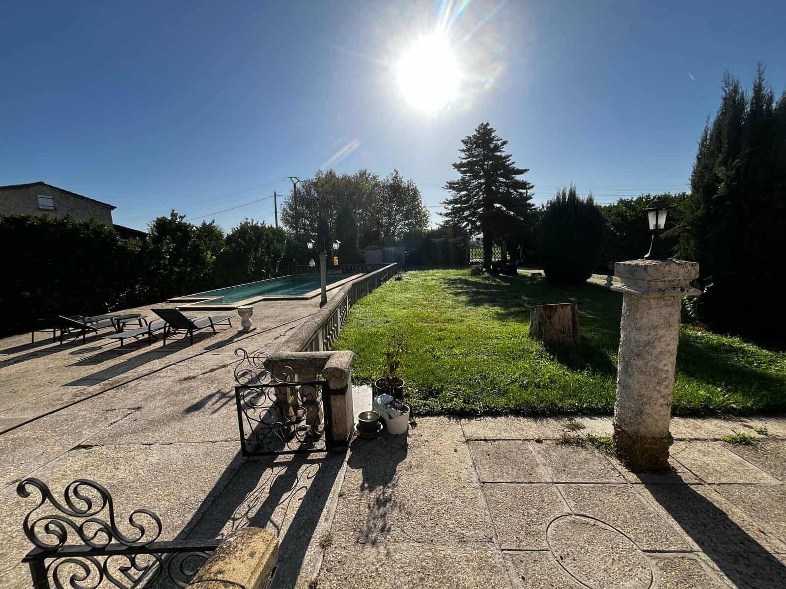 Un espacio exterior soleado con piscina, sillones de descanso y un pilar de piedra.