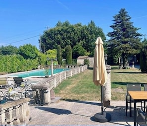 A poolside area with a stone deck, lounge chairs, and an umbrella. - Villa Papillon (Monteux)