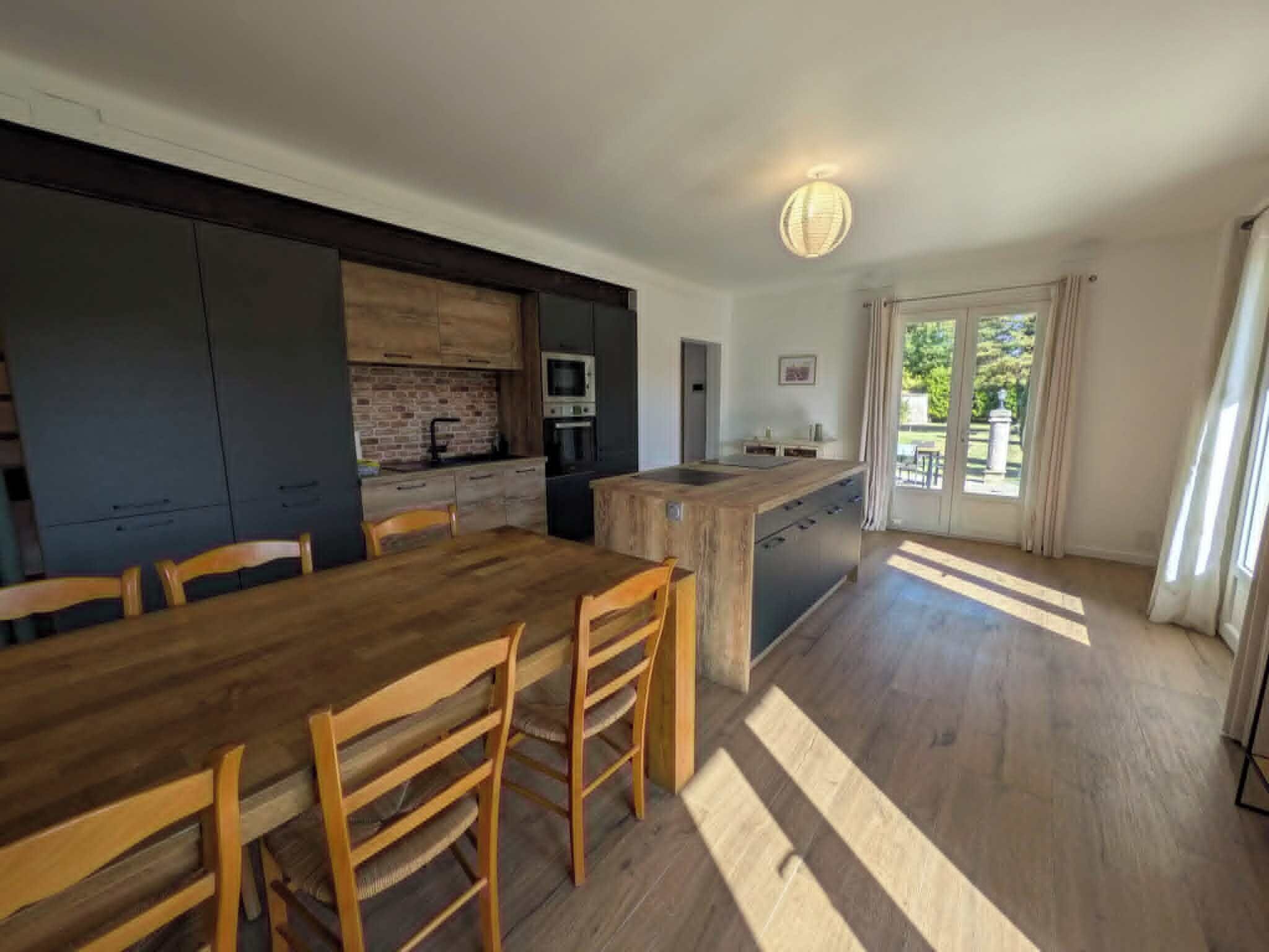 Une cuisine moderne avec des meubles de rangement aux couleurs sombres, une table à manger en bois et des chaises.