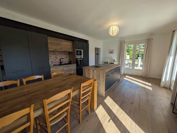 A modern kitchen with dark cabinetry, a wooden dining table, and chairs. - Villa Papillon (Monteux)