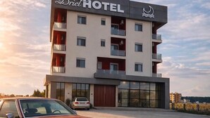 A hotel building with a sign reading 'Brill HOTEL' and a classic red car parked in front.