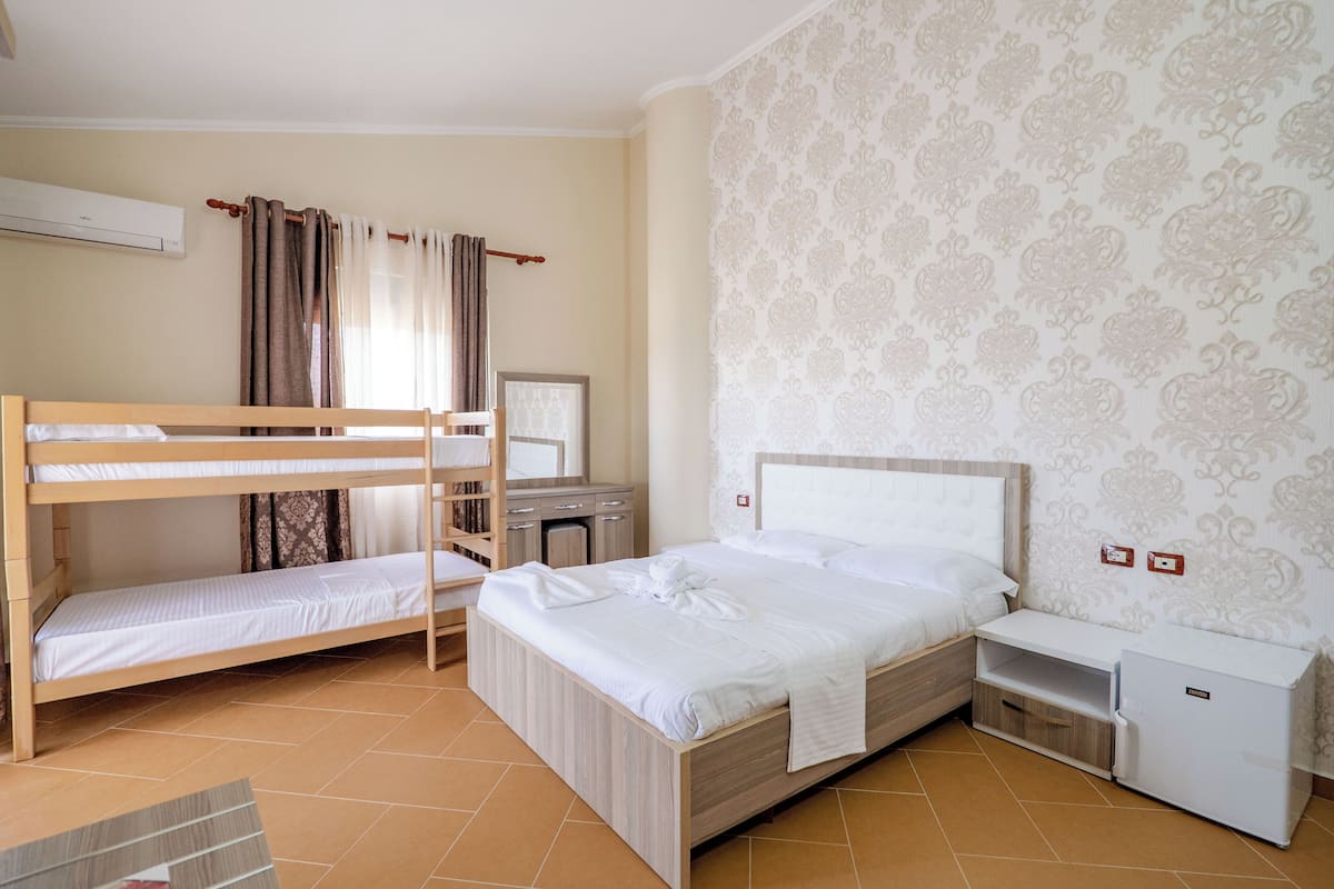 Een hotelkamer met een stapelbed, een bureau met stoel, een klein kastje en een wandairconditioner.