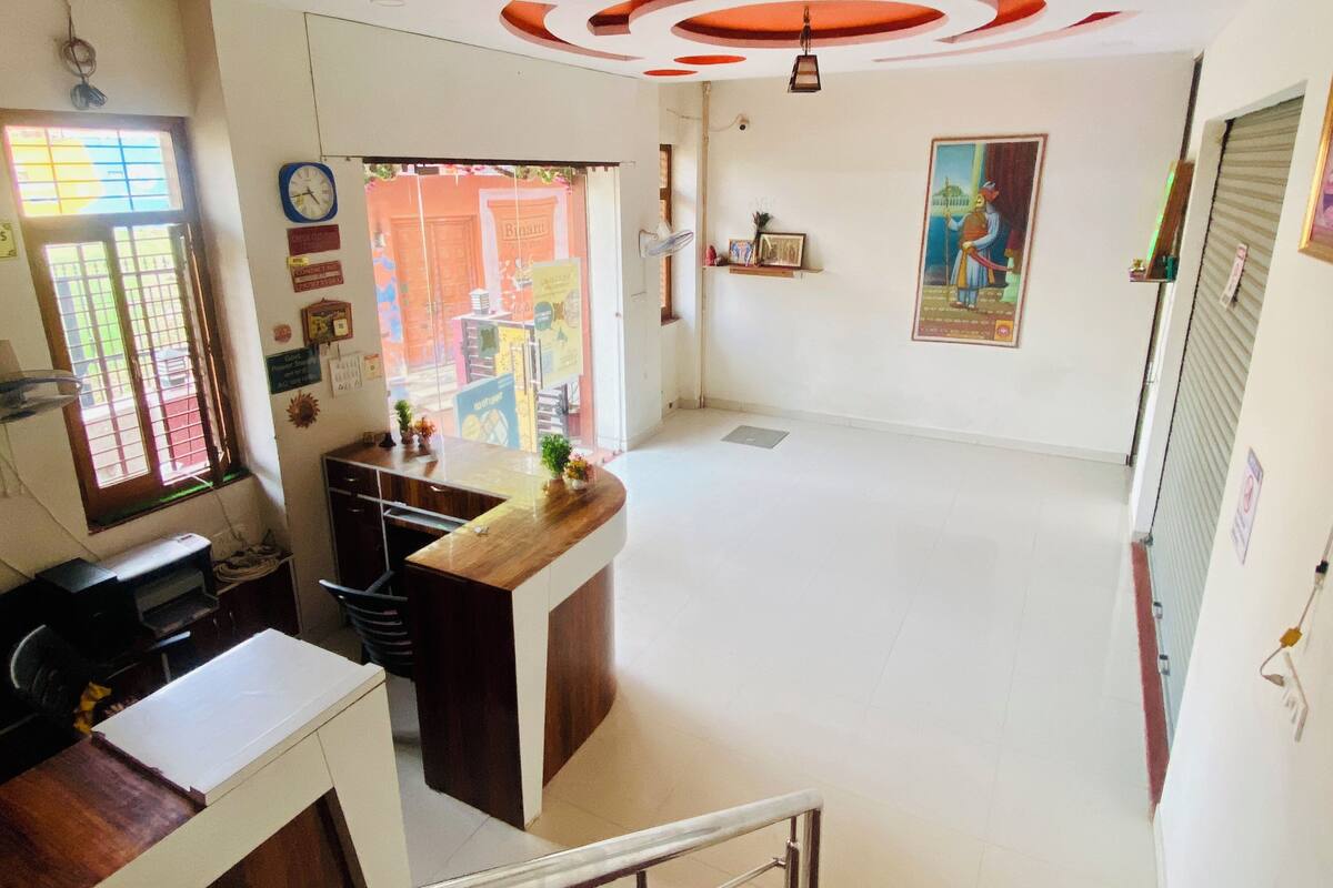 Une pièce spacieuse avec un comptoir d’accueil en bois, une grande fenêtre avec des barreaux, un ventilateur de plafond et un tableau accroché au mur.