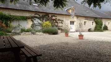 A stone building with a gravel courtyard, a wooden bench, and potted plants.