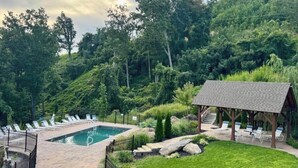 Ein Poolbereich mit Liegestühlen und einem Pavillon, umgeben von üppiger Vegetation.