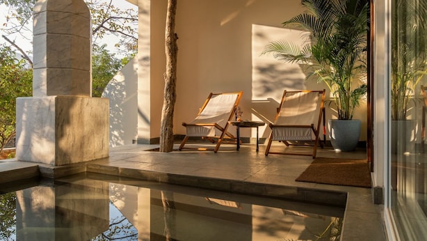 A pool area with two lounge chairs, a stone pillar, and a large potted plant. - Vihara Udaipur (Udaipur)