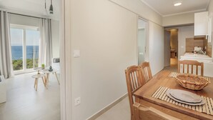 A modern dining area with a wooden table, chairs, and a view of the sea through large windows. - Restia tower apartments (Zakynthos)