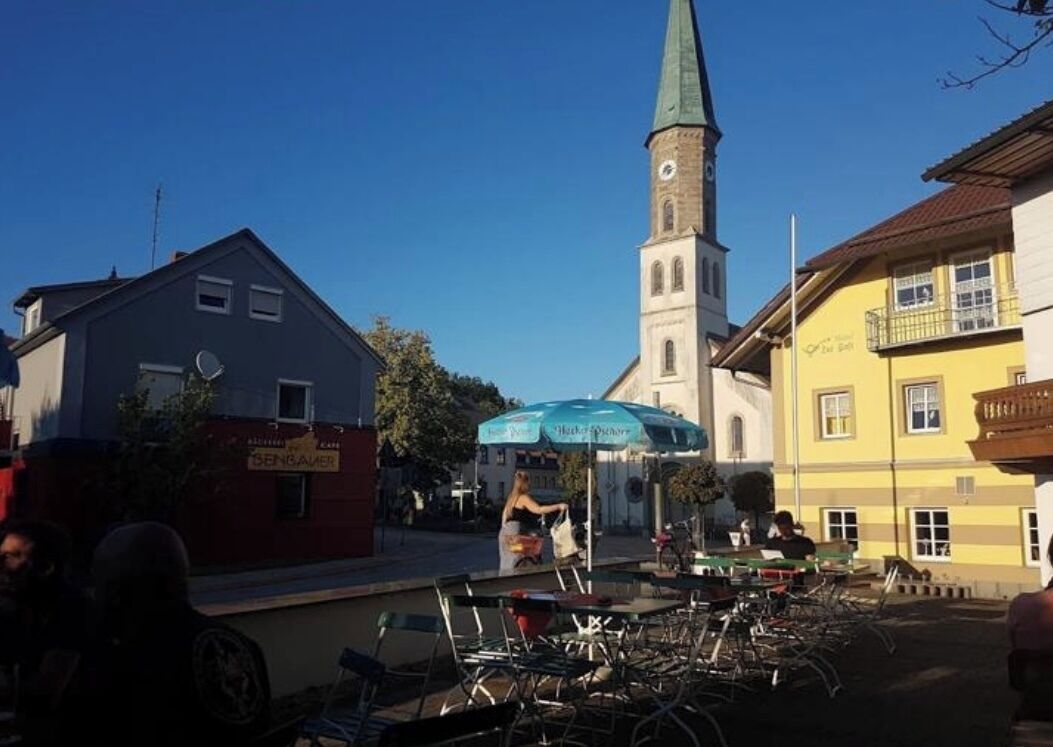 A town square with a church steeple, outdoor seating, and bicycles.