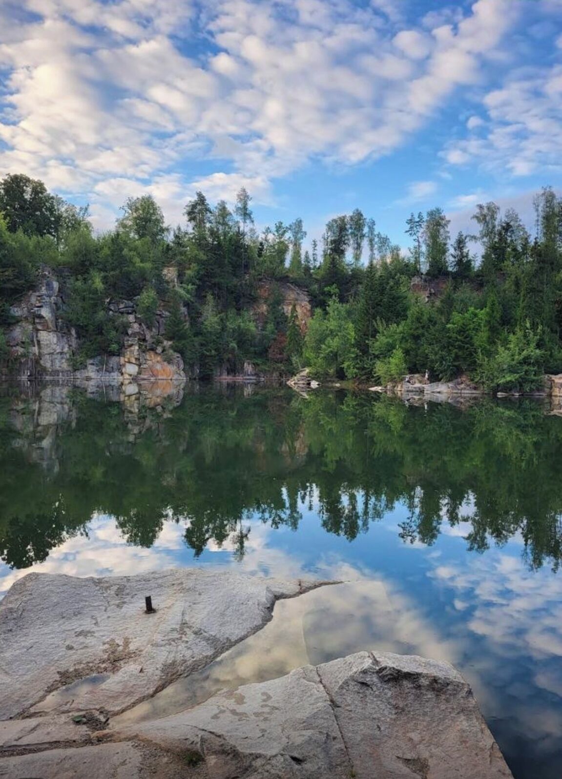 A calm lake with clear reflections of the surrounding trees and sky.