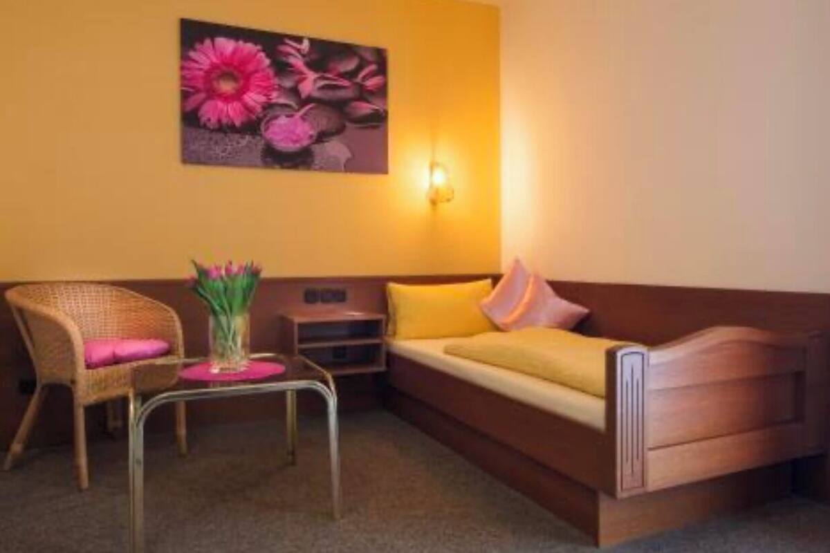 A small, cozy room with a wooden sofa, a wicker chair, and a small table with a vase of flowers.