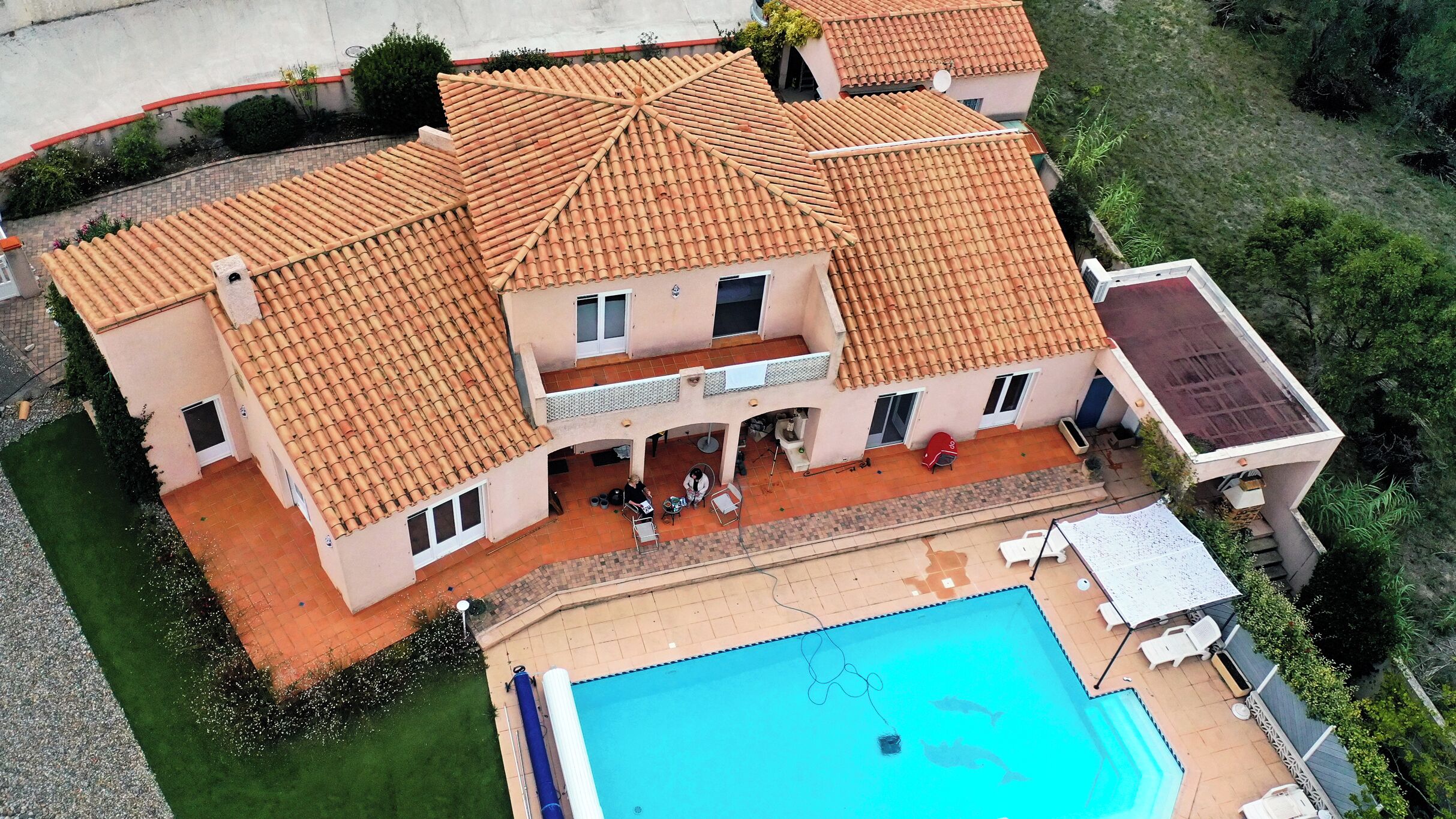 A two-story house with a tiled roof, a swimming pool, and a covered patio area.