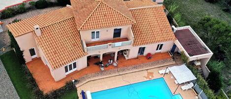 A two-story house with a tiled roof, a swimming pool, and a covered patio area.