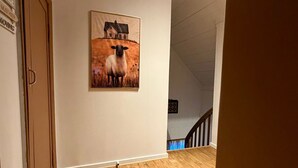 A hallway with wooden flooring, a painting of a sheep and a house, and a staircase in the background. - Cabane à Oppdal (Trøndelag)
