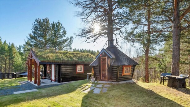 A log cabin with a thatched roof and a separate wooden structure, surrounded by a forested area. - Cabane à Oppdal (Trøndelag)