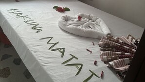 A neatly made bed with a white bedspread, a towel, and a decorative arrangement of leaves spelling "HANA NAATA". - Spacious Deluxe Double Room With AC (Paje)