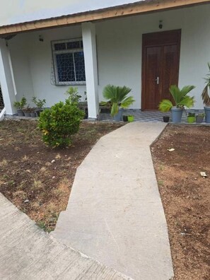 A concrete pathway leading to a building with a wooden door and a window with a metal grill. - Spacious Deluxe Double Room With AC (Paje)