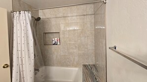 Une salle de bain avec une baignoire, un rideau de douche et une petite étagère contenant des articles de toilette.