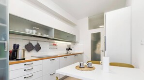 A modern kitchen with white cabinets, a stainless steel kettle, and a dining area with a white table and chairs. - Greco Heritage Suite in Milan (Milan)