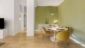 A modern living room with a dining area, featuring a flat-screen TV, a white console table, and a round dining table with yellow chairs. - Greco Heritage Suite in Milan (Milan)