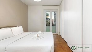A modern bedroom with a large bed, a small table with a towel and a cup, and a view of a balcony with greenery. - Greco Heritage Suite in Milan (Milan)
