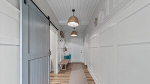 Un couloir doté d’un plancher en bois, de murs blancs, d’un banc et de deux lampes suspendues.